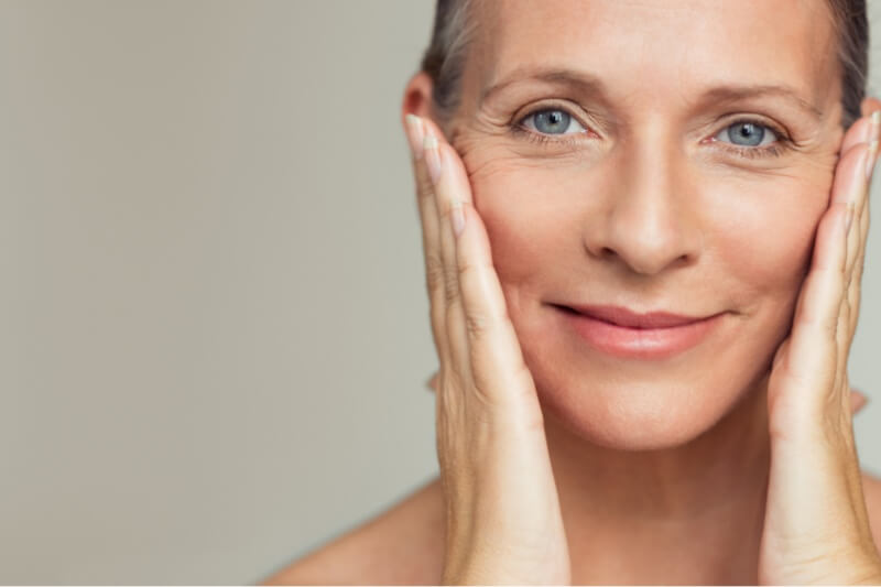Dermal fillers | An older woman looking at the camera and touching her face with her hand.