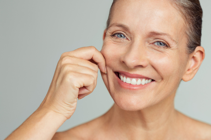 Dermal fillers | A woman smiling and pinching her cheek with her fingers.