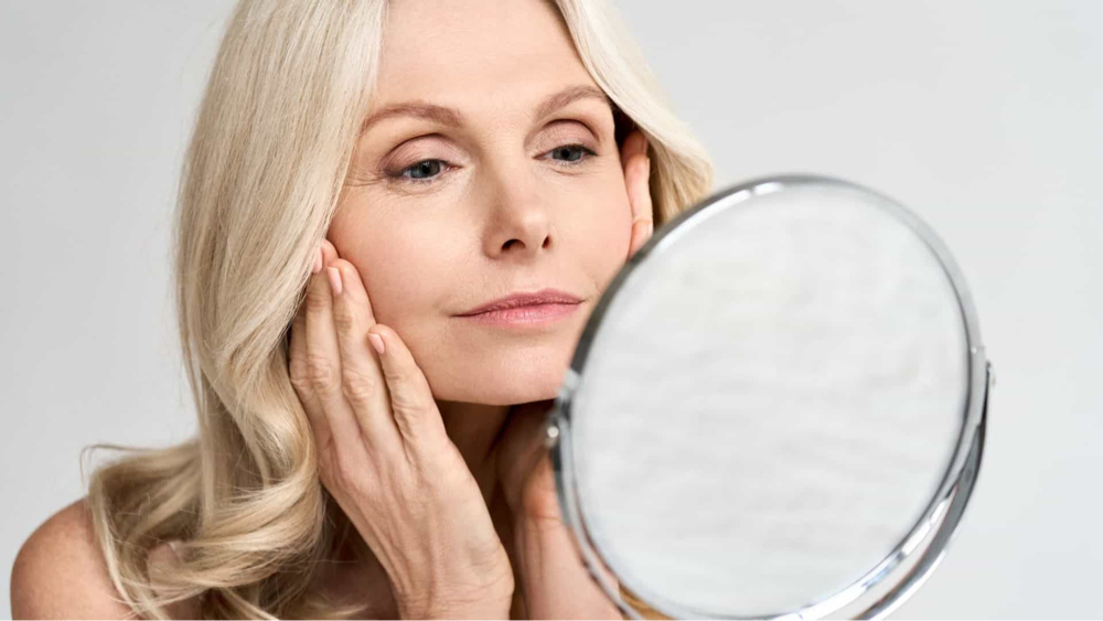 Profhilo | An image of a middle-aged white blonde lady looking herself from the mirror.