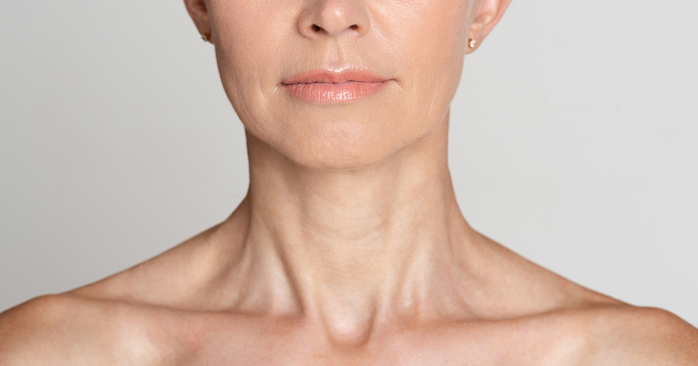 Minimally Invasive Neck Lift | Half face portrait of mature woman with wrinkled neck, grey background, crop